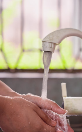 A close-up imagery depicting hands being washed beneath a running water faucet, highlighting personal hygiene, cleanliness, and the importance of maintaining germ-free practices as part of daily routines.の写真素材