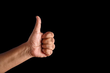 A close-up of a hand performing a thumbs-up gesture against a solid black background, symbolizing...