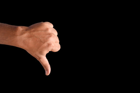 A hand making a thumbs-down gesture, captured close-up against a solid black backdrop.