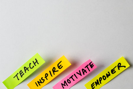 Four colorful sticky notes display motivational words like Teach, Inspire, Motivate and Empower, forming a compelling visual symbol of encouragement, growth mindsets, and personal development.の写真素材
