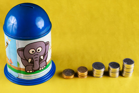 A children-themed piggy bank featuring an elephant design next to stacks of coins. Vibrant yellow backdrop enhances the colorful appeal, symbolizing saving money, growth, and financial planning in a visually appealing composition.の写真素材