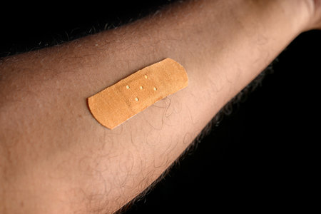 A close-up view of a medical bandage applied on a person's arm against a dark background, symbolizing healing, care, and medical equipment.の写真素材