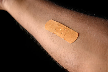 A close-up view of a medical bandage applied on a person's arm against a dark background, symbolizing healing, care, and medical equipment.の写真素材
