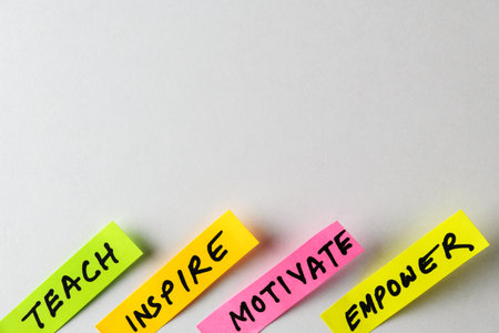 Four colorful sticky notes display motivational words like Teach, Inspire, Motivate and Empower, forming a compelling visual symbol of encouragement, growth mindsets, and personal development.の写真素材