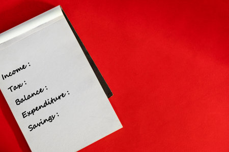 A financial planning notebook displaying income, tax, balance, expenditure, and savings, set on a vibrant red background. Perfect for illustrating budgeting, finance management, and organization concepts.の写真素材