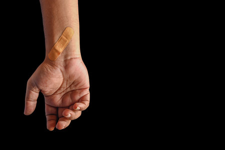 A close-up image of a hand with a small adhesive bandage on the wrist, highlighting themes of care,...