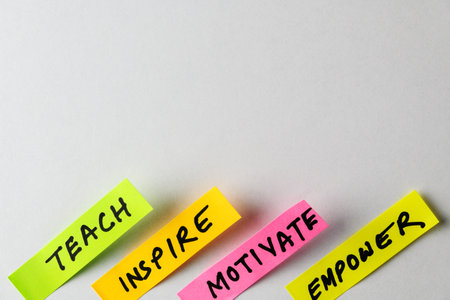 Four colorful sticky notes display motivational words like Teach, Inspire, Motivate and Empower, forming a compelling visual symbol of encouragement, growth mindsets, and personal development.の写真素材