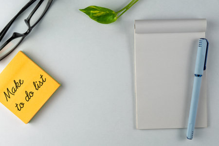 Bright and neat desk arrangement featuring a yellow sticky note with a motivational to-do list, accompanied by a pen and a notepad, promoting productivity and planning efficiency.の写真素材