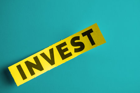 The image displays the word 'Invest' in bold text on a yellow strip placed on a blue background, symbolizing finance, investment opportunities, and economic growth while highlighting focus on modern design.の写真素材