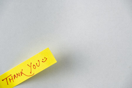 Bright yellow note with a handwritten thank you message and a smiley face composed on a soft, neutral surface. Represents gratitude, positivity, and personal expression.の写真素材
