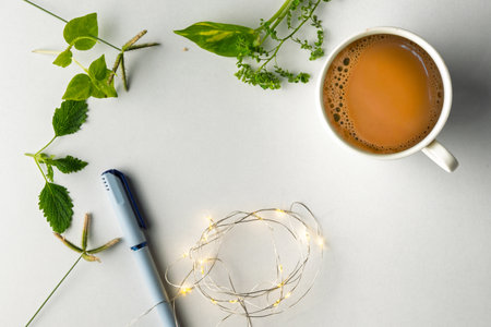 A flat-lay arrangement featuring a cup of tea, green plants, a blue pen, and decorative fairy lights...