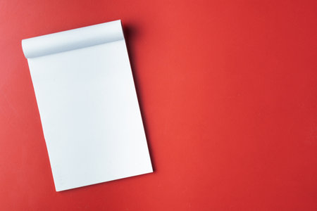 A minimalistic scene showcasing a blank white notepad lying on a vibrant red surface, symbolizing creativity, design, and organization, ideal for presentations, writing, and artistic purposes.の写真素材