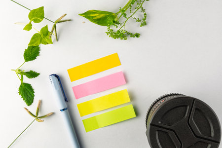 Vibrant sticky notes in pink, yellow, and green tones placed next to a pen and surrounded by fresh...