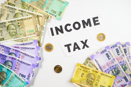 A composition featuring Indian rupee banknotes and coins surrounding the text 'Income Tax', symbolizing financial management, tax obligations, and monetary responsibility in India.の写真素材