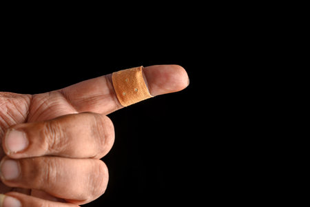 Close-up of a person's hand with an injured finger wearing a bandage, isolated against a black...