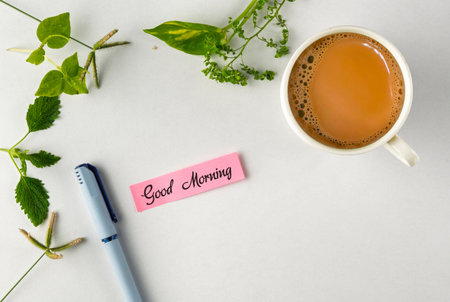 A warm start to the day featuring a cup of hot tea, fresh greenery, and a note saying "Good Morning," providing a feeling of positivity and calm.の写真素材