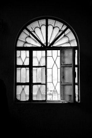 Black and white photograph featuring a vintage arched window with textured and patterned glass panes, depicting a nostalgic atmosphere with symbolic and artistic detail.の写真素材
