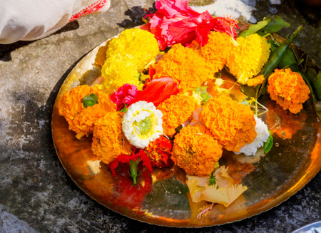 A colorful arrangement of fresh flowers placed on a golden tray. Representing tradition, celebration, and decorative purposes in cultural or spiritual settings. Marigolds and hibiscus are particularly prominent.の写真素材
