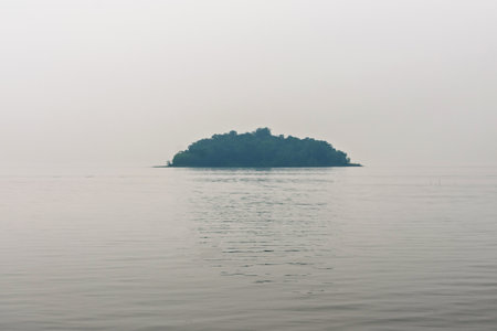 A serene view of a small isolated island surrounded by vast calm waters on a misty day, evoking feelings of solitude and tranquility.の写真素材