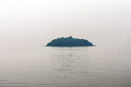 A serene view of a small isolated island surrounded by vast calm waters on a misty day, evoking feelings of solitude and tranquility.の写真素材