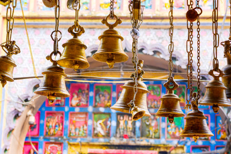 Golden bells hang elegantly, providing a tranquil ambiance against a colorful backdrop of traditional Indian artwork, evoking a sense of spirituality and cultural heritage.の写真素材