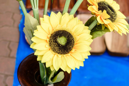 A display of vibrant artificial sunflowers with realistic yellow petals placed in a vase. The composition features contrasting textures and colors that create an elegant decoration and cheerful atmosphere.の写真素材