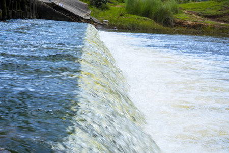 A tranquil scene of water cascading over a small dam, surrounded by lush greenery, illustrating the...