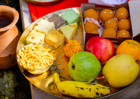 A vibrant arrangement of traditional Indian fruits and sweets displayed on a brass plate, symbolizing generosity and festivity, often accompanying rituals and celebrations as offerings to the divine.の写真素材