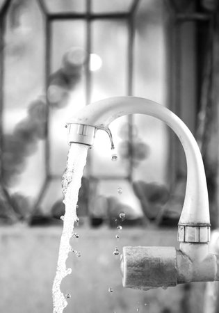 Black-and-white photo of a faucet dispensing water, captured with focus on water droplets for a minimalist and environmentally conscious theme.の写真素材