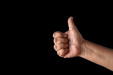 A close-up of a hand performing a thumbs-up gesture against a solid black background, symbolizing positivity, approval, and success. The isolated setting emphasizes the message of encouragement and agreement.の写真素材