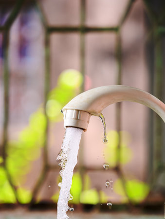 Close-up view of a water tap pouring fresh water with nature as a blurry background. Highlights hydration, nature, and freshness.の写真素材