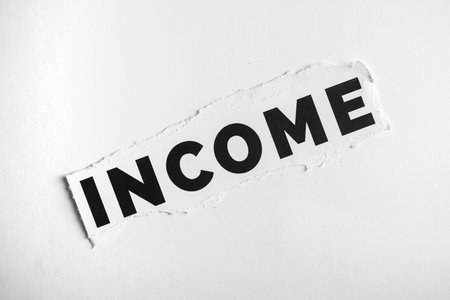 The image displays the word 'INCOME' printed in bold letters, featured on a torn piece of paper set against a white background, symbolizing financial concepts and monetary themes.の写真素材