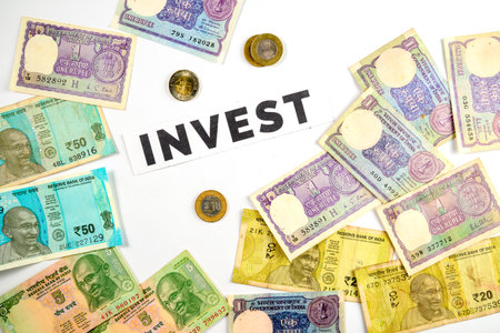 Collection of Indian currency notes and coins arranged around the word invest, symbolizing financial...