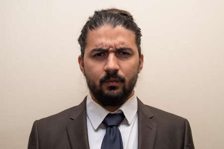 Man in a suit and blue tie with doubt or anger expression, with a single color background