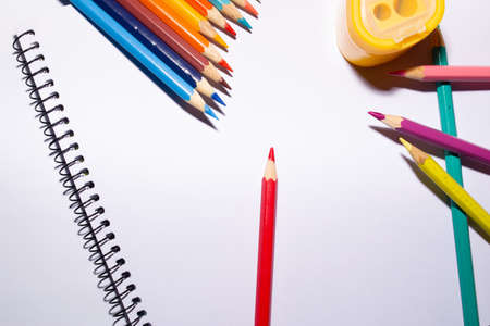a sketchbook, colored pencils and a sharpener on white backgroundの写真素材