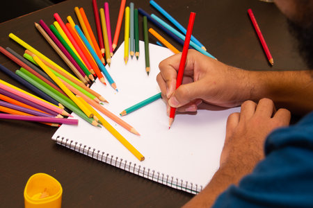 A man's hands drawing with colored pencils on the white panel on the wooden tableの写真素材