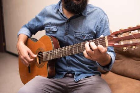 Man dressed in casual clothes playing guitar, sitting on an armchair in a roomの写真素材