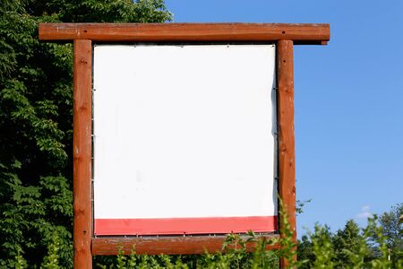 whiteboard, empty billboard in wood frame on blue sky and trees backgroundの写真素材