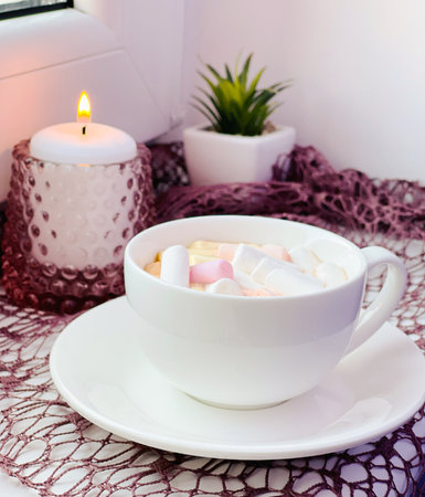 burning candle and a cup with marmallows on the windowの写真素材