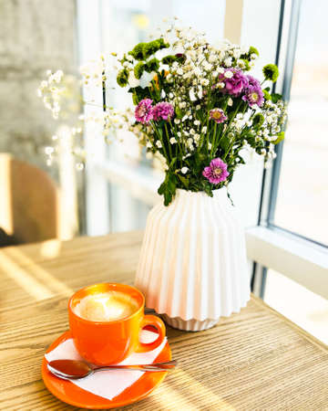 white vase with wildflowers and americano, on a table in a cafeの写真素材