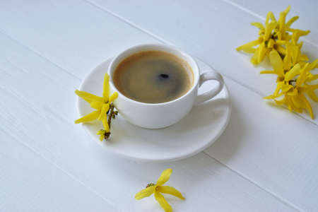 cup of coffee and yellow forsythia on a white wooden table