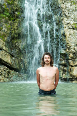 man stands waist deep in a pond near the waterfallの写真素材