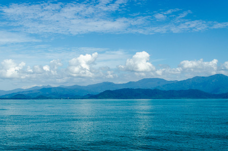 Horizontal of Seascape including Forest Mountain, Blue Sky and Wave of Water Foam in Ocean.の写真素材