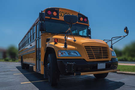 Low front right angle view of yellow American public school bus showing door with sun directly...
