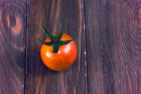 small red cherry tomato with small part of stem sitting on rustic wooden table topの写真素材