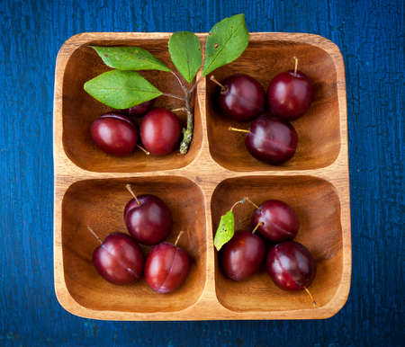 Plums in a wooden bowl on a blue wooden backgroundの写真素材