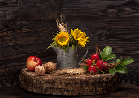 Flowers sunflower, wild rose, apple and walnuts on wooden board. Autumn Still Lifeの写真素材
