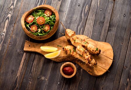 Shish kebab turkey fillet on bamboo skewers and arugula salad with tomatoes and pine nuts, top view, flat layの写真素材