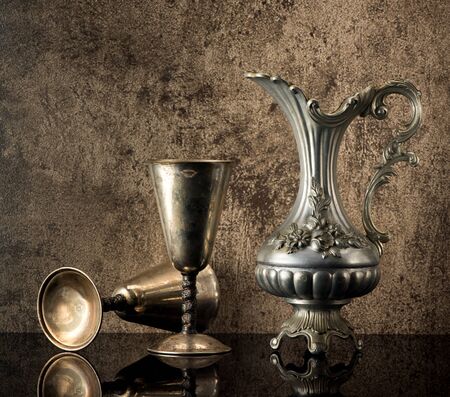 Still life with Ancient jug for wine and silver goblets on a stone backgroundの写真素材