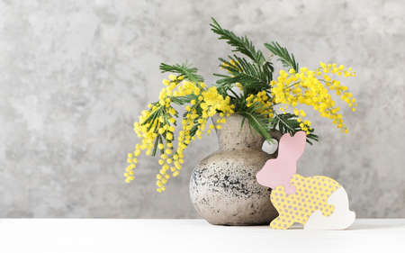 Happy Easter background with beautiful spring bouquet mimosa in vase and wooden bunny. Easter concept with copy space.の写真素材